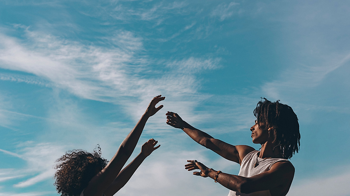 Two people raise their arms toward the sky, silhouetted against a blue sky with wispy clouds.