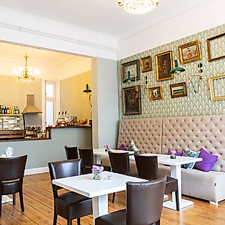 Stilvoll eingerichtetes Café Hermitage in Hamburg Eppendorf mit gemütlicher Sitzbank, Bilderwand und Blick in die offene Küche