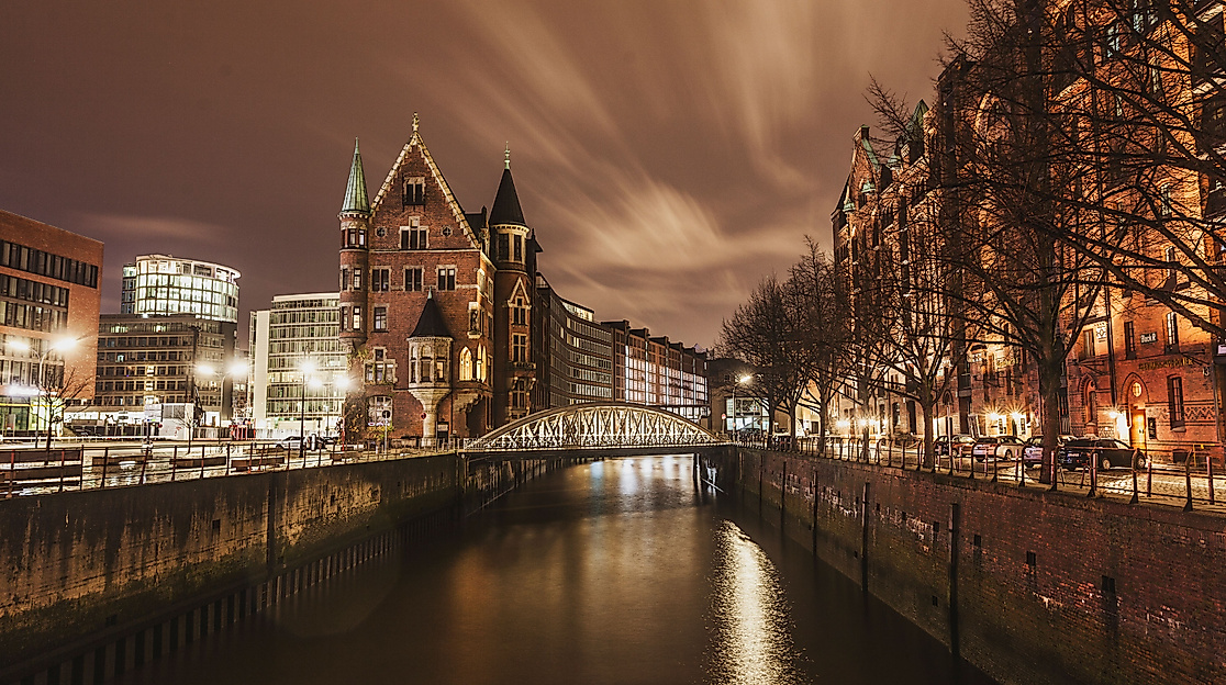 Beleuchtete Speicherstadt bei Nacht mit spiegelndem Wasserlauf und Bäumen am Ufer