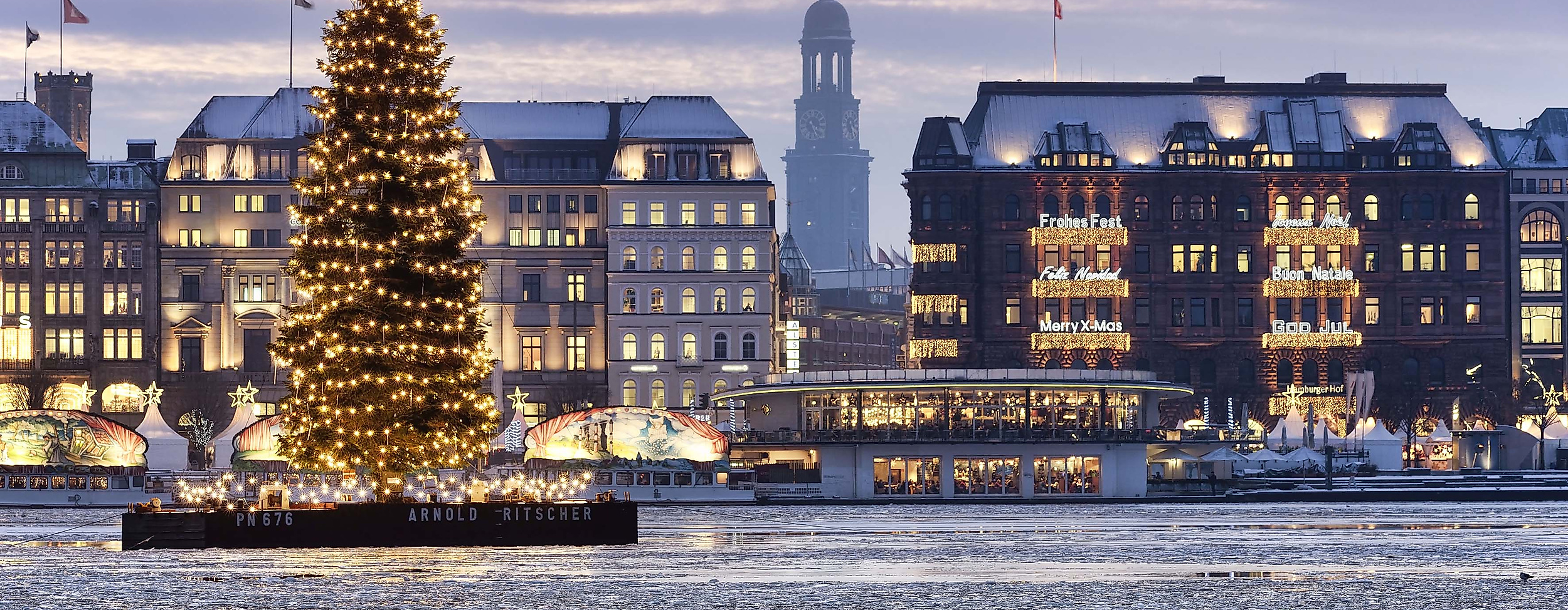 Beleuchteter Weihnachtsbaum auf der winterlichen Binnenalster vor verschneiter Hamburger Kulisse