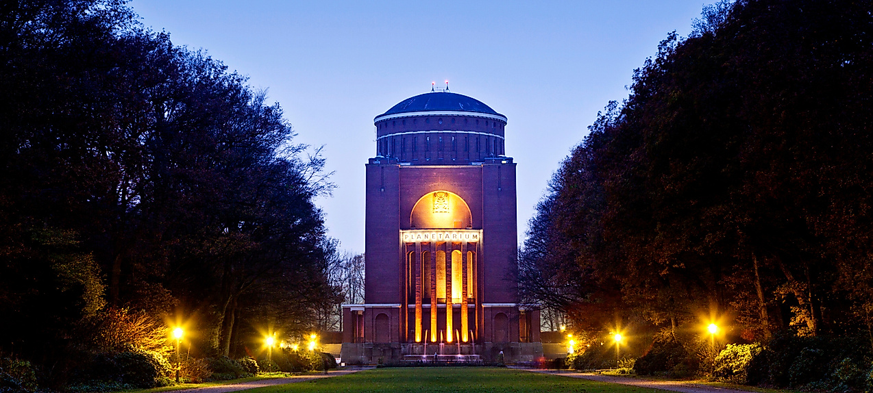 Beleuchtetes Planetarium Hamburg am Abend, eingerahmt von Bäumen und mit Blick auf den Vorplatz