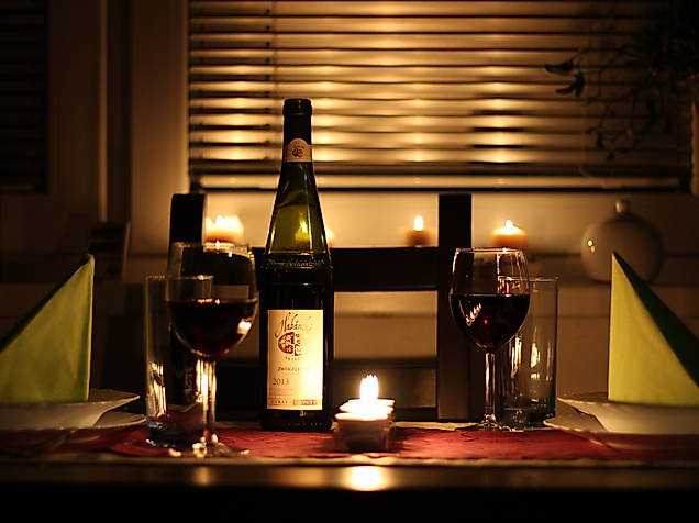 Romantisch gedeckter Tisch mit Kerzenlicht, Rotwein und Weinflasche für ein Candle-Light-Dinner
