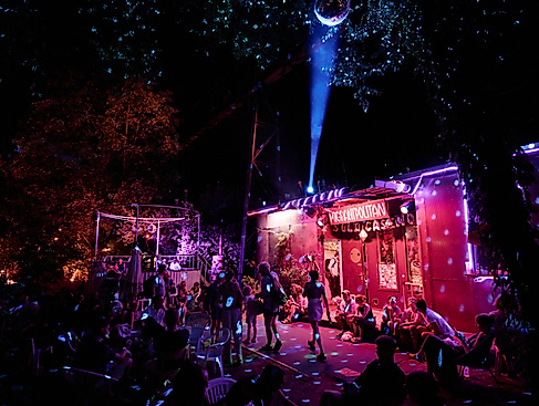 Party vor dem Migrantpolitan. Besucher*innen bewegen sich in pinkem Licht unter einer Discokugel.