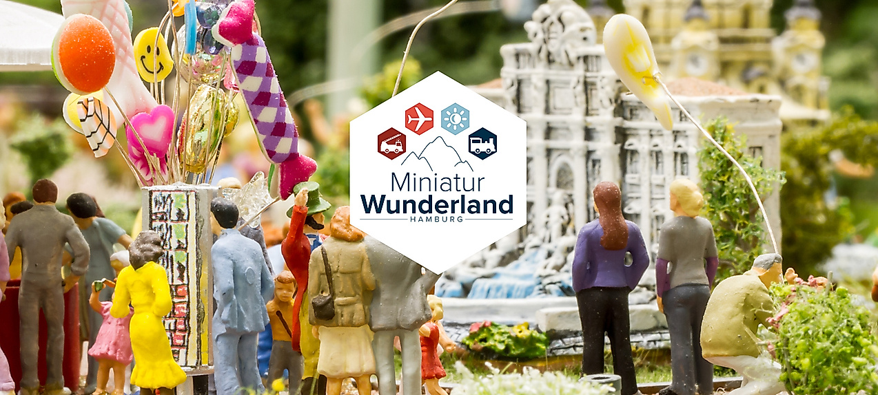 Bunte Miniaturszene mit Menschen, Luftballons und Modellgebäuden im Miniatur Wunderland Hamburg mit Logo des Miniatur Wunderlands Hamburg mit Symbolen für Bahn, Flugzeug, Sonne, Schiff und Lkw