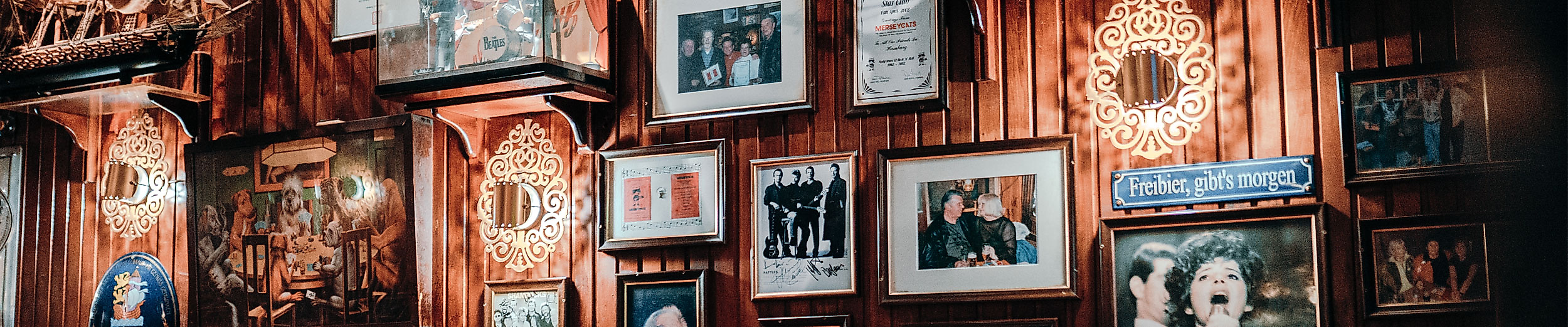 Gemütliche Kneipe mit rot gepolsterter Sitzbank, Holztischen und Wänden voller gerahmter Fotos