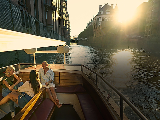 Drei Personen genießen Bootstour durch Hamburgs Speicherstadt bei Sonnenuntergang – historische Backsteinfassaden am Wasser