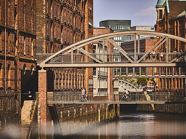 Historische Stahlbrücke in der Speicherstadt vor roten Backsteinfassaden, gespiegelt im Wasser des Fleets