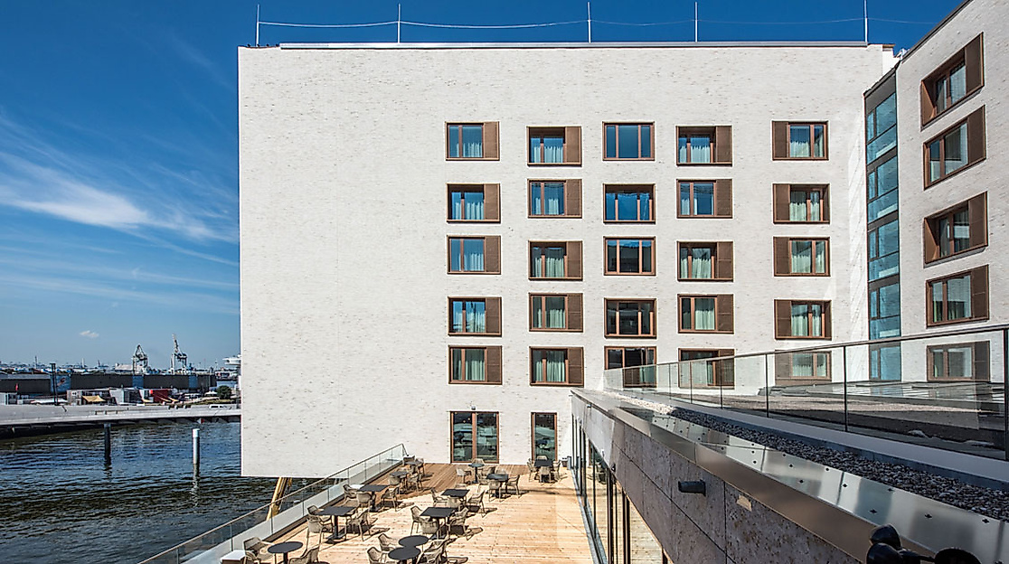 Barrierefreies JUFA Hotel Hamburg mit heller Fassade, Außenterrasse und Blick auf den Hafen.