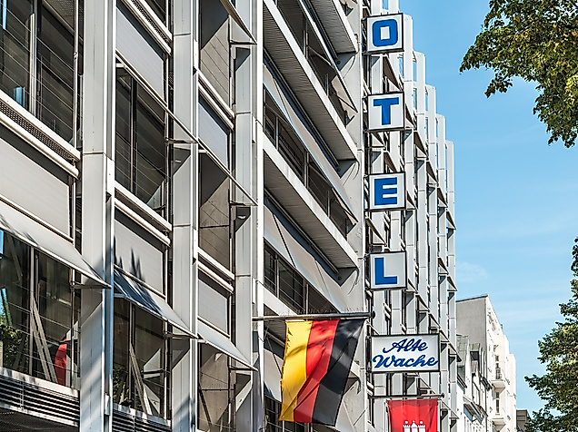 Mehrstöckiges Gebäude mit senkrechtem Hotelschild, deutscher und Hamburg Flagge