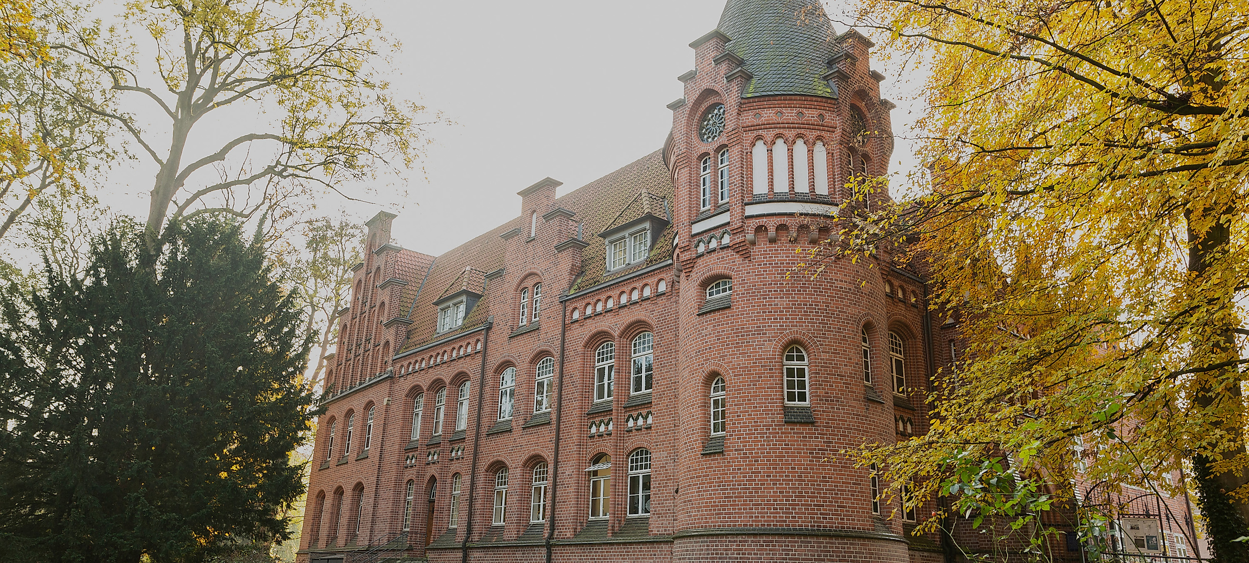 Backsteinfassade des Bergedorfer Schlosses in Hamburg, umgeben von herbstlichen Bäumen und Weg im Vordergrund