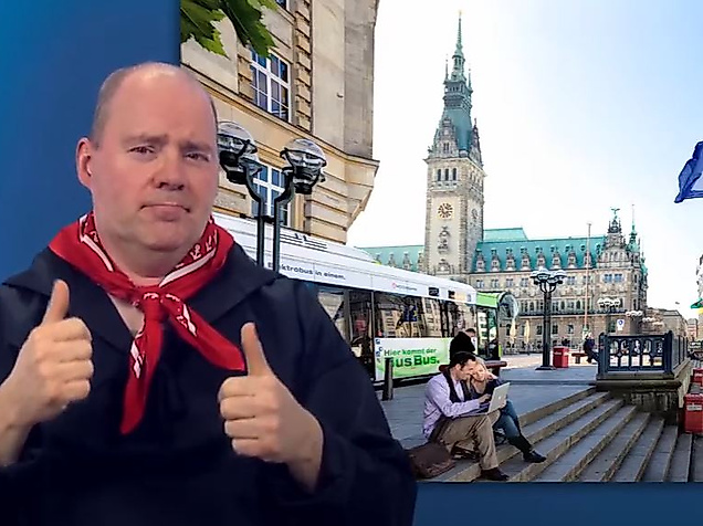 Mann gebärdet vor dem Hamburger Rathaus – barrierefreie Infos zum Nahverkehr.