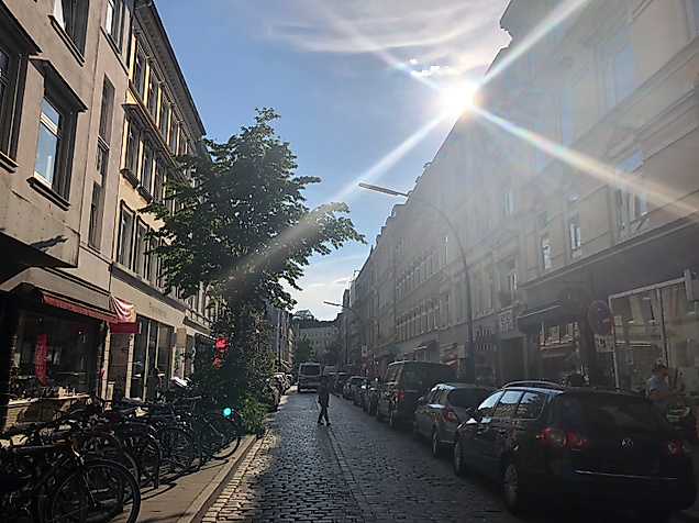 Sonnenlicht fällt auf die lebendige Bahrenfelder Straße mit kleinen Läden, Cafés und geparkten Fahrrädern