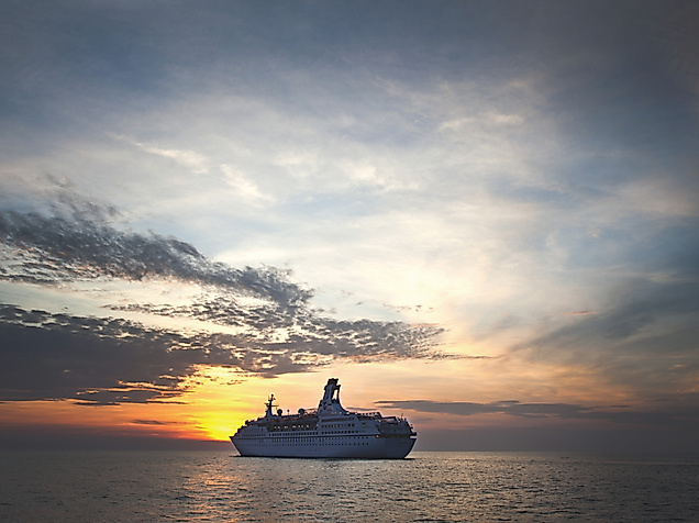 Kreuzfahrtschiff Astor bei Sonnenuntergang auf ruhiger See unter teils bewölktem Himmel