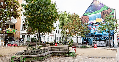Platz im Hamburger Schanzenviertel mit Sitzbänken, Bäumen und farbenfrohem Wandgemälde an einer Giebelfassade