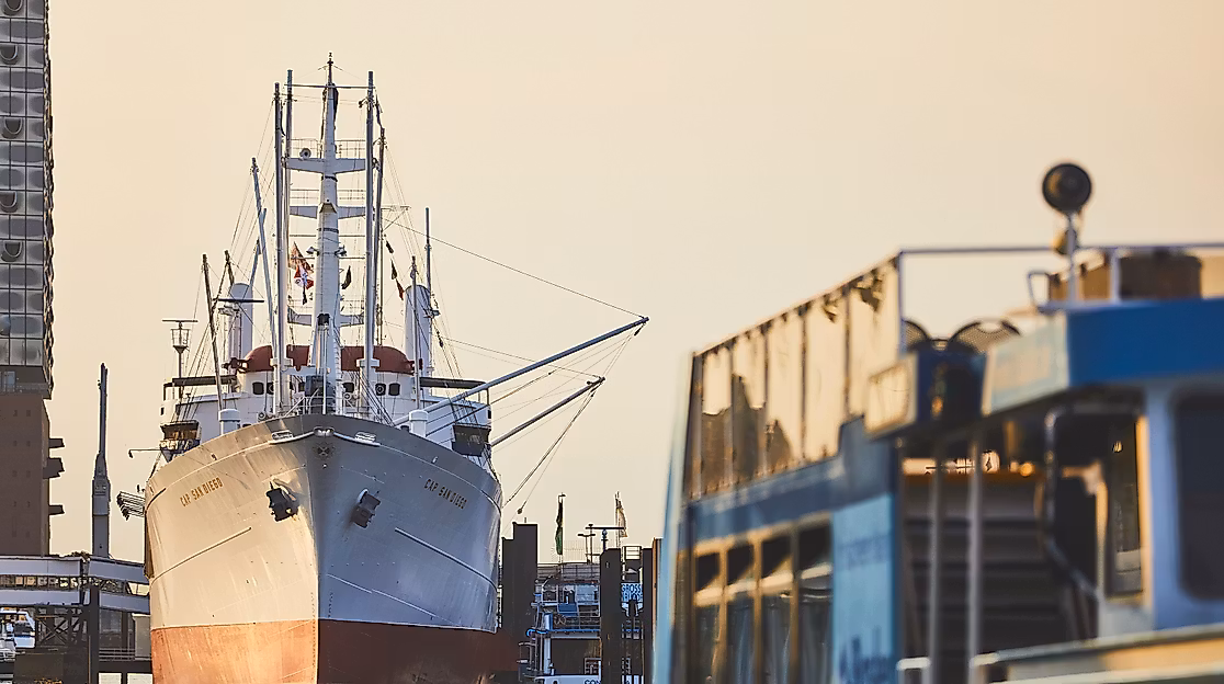 Bugansicht der Cap San Diego im Hamburger Hafen bei Sonnenaufgang, rechts eine Hafenfähre 
