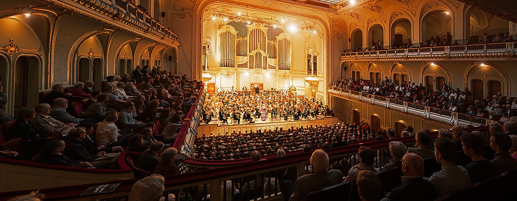 Festlich beleuchteter Opernsaal mit großem Orchester und Publikum