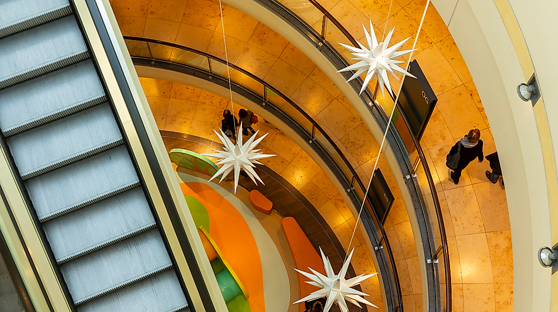 Innenansicht des Alstertaler Einkaufszentrums mit Rolltreppe, runden Galerien und festlicher Beleuchtung.