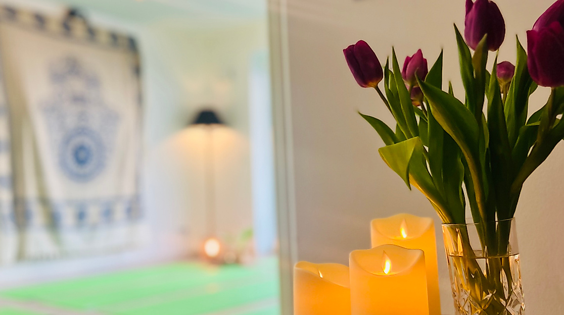 Achtsamkeitsraum mit Kerzen und Blumen. Im Hintergrund liegen Yogamatten für das Yoga- und Achtsamkeitswochenende.