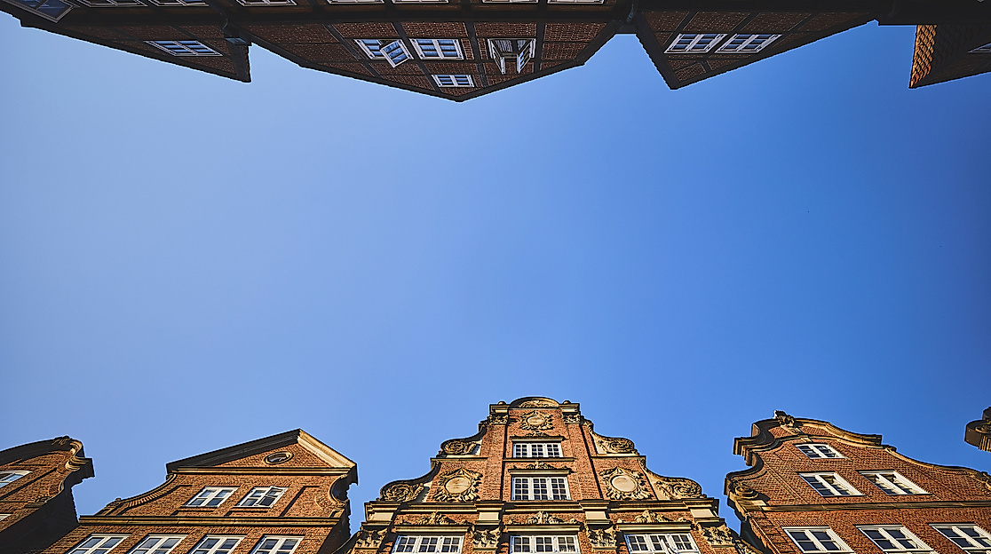 Blick nach oben auf historische Giebelhäuser im Komponistenviertel Hamburg vor klarem, blauem Himmel.