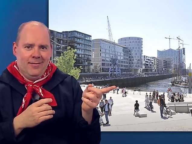 Mann gebärdet vor sonniger Promenade in der Hamburger HafenCity – barrierefreie Infos zum modernen Stadtteil.