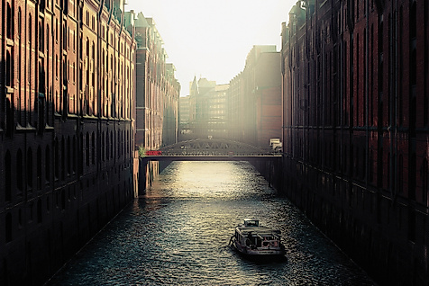 Schmale Wasserstraße der Speicherstadt im Gegenlicht mit reflektierendem Wasser und Backsteinfassaden