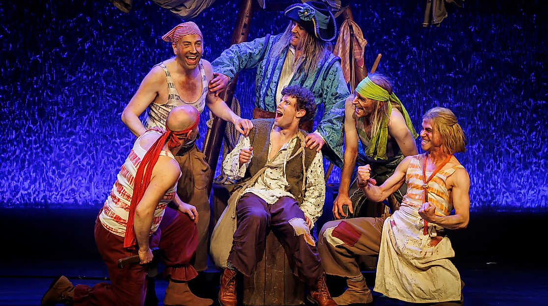 Szenenbild Der kleine Störtebeker: Störtebeker umgeben von anderen Menschen in bunten Kostümen. 