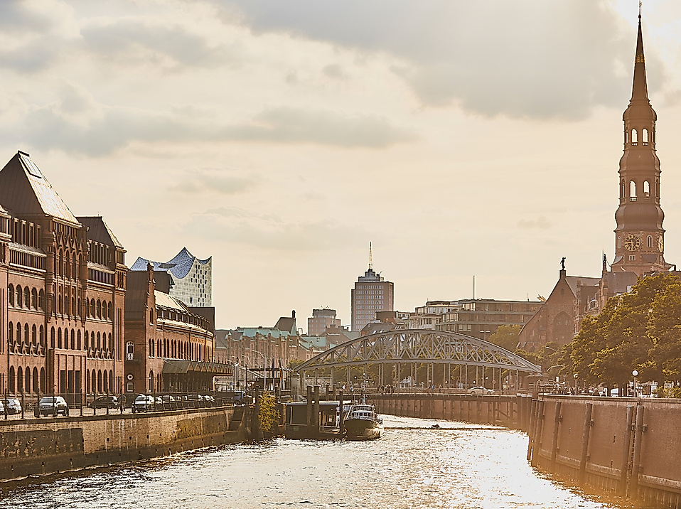 Blick auf Nikolaikirche, Speicherstadt und Elbphilharmonie in Hamburg bei warmem Abendlicht über dem Fleet