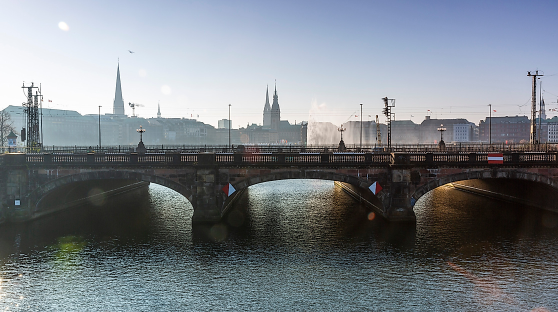 Blick auf die Lombardsbrücke in Hamburg mit Alsterwasser im Vordergrund und Stadtpanorama im Gegenlicht