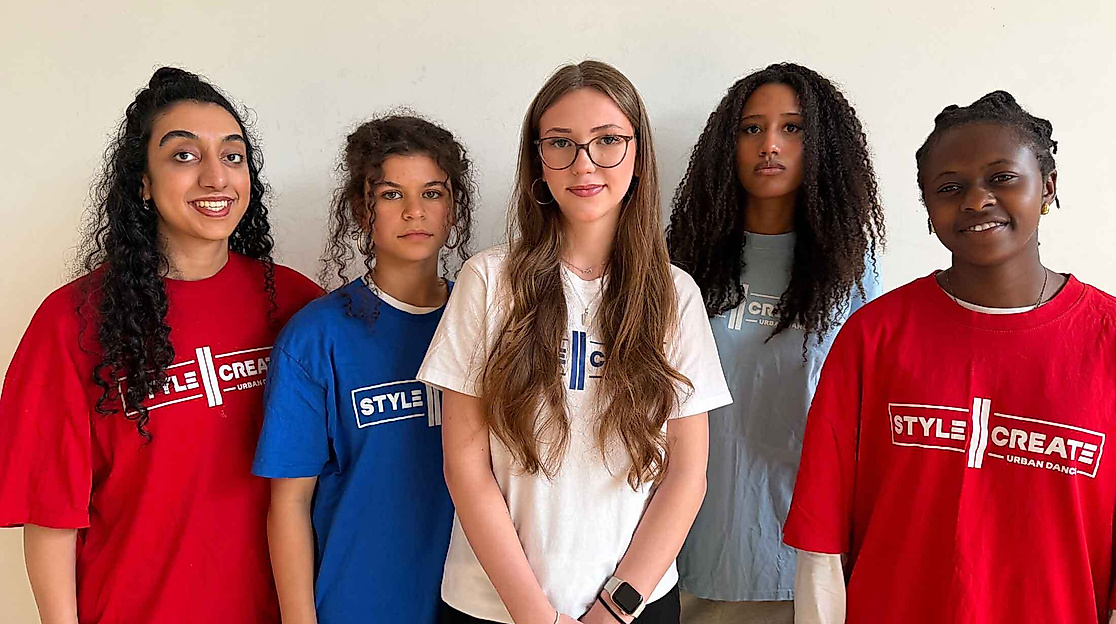 Fünf Personen mit unterschiedlichen Haarlängen und -strukturen tragen bunte T-Shirts mit dem Schriftzug "STYLE CREATE" und stehen vor einer hellen Wand.