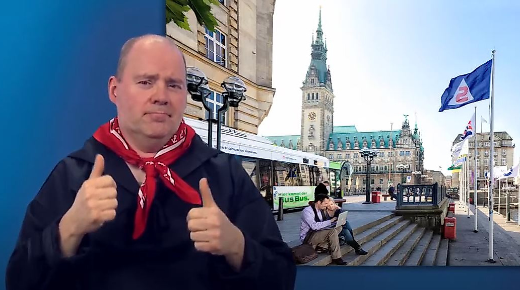 Mann gebärdet vor dem Hamburger Rathaus – barrierefreie Infos zum Nahverkehr.