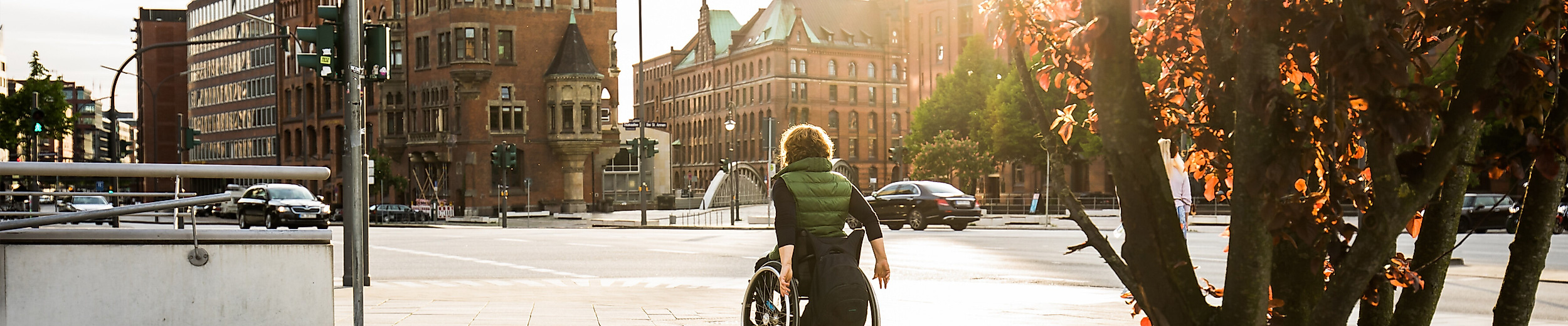 Rollstuhlfahrer unterwegs auf barrierefreiem Weg in der Hamburger Innenstadt bei Sonnenuntergang.