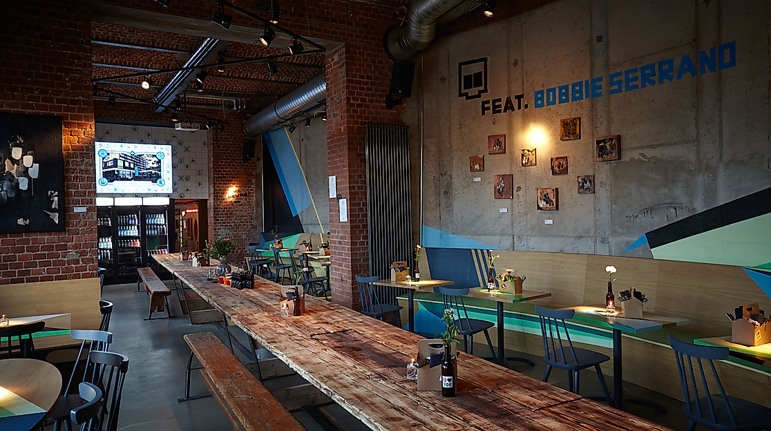 Rustikales Brauhaus mit langer Holztischtafel, Wandkunst und gemütlicher Beleuchtung im ÜberQuell Hamburg