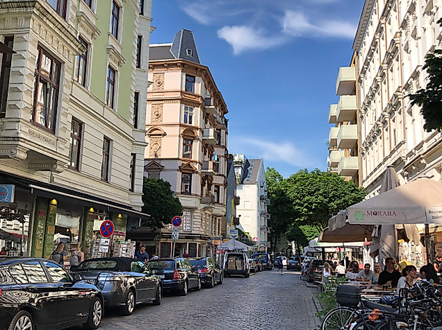 Lebendige Schanzenstraße in Hamburg mit Altbauten, kleinen Läden, Cafés und Passant:innen bei Sonnenschein