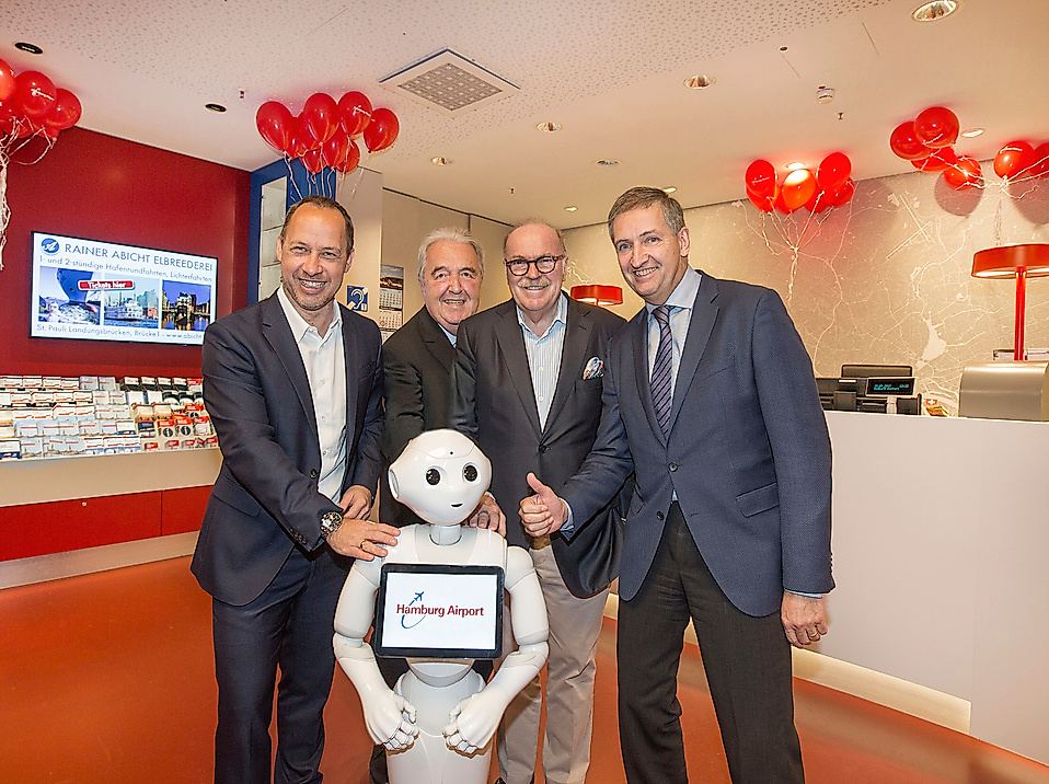 Vier Männer posieren mit humanoidem Roboter in einem festlich dekorierten Hamburg Tourismus-Besucherzentrum