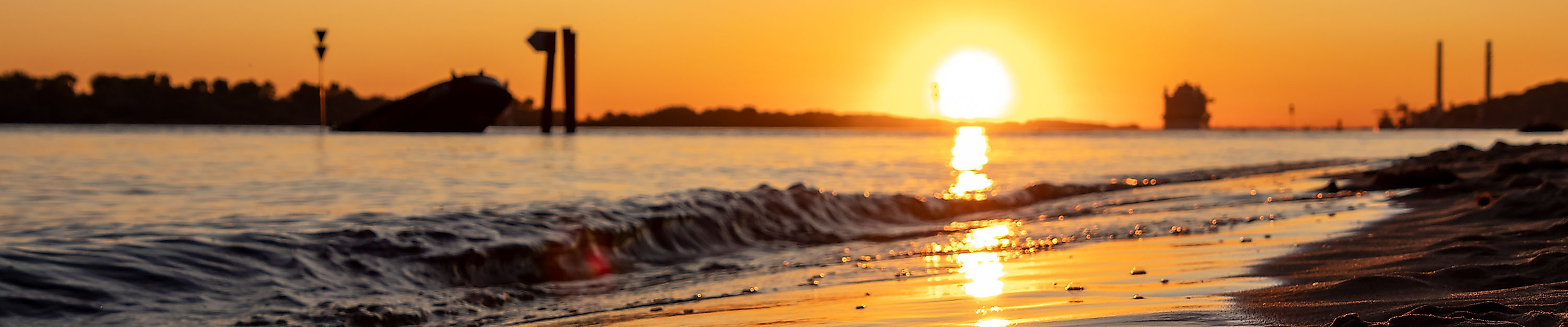Sonnenuntergang am Elbstrand in Hamburg mit Blick auf glitzerndes Wasser und vorbeiziehendes Containerschiff