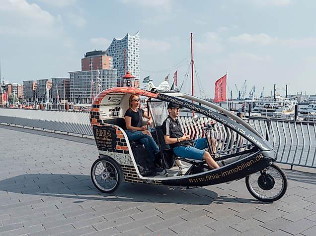 Rikscha mit zwei Fahrgästen an den Landungsbrücken, im Hintergrund die Elbphilharmonie
