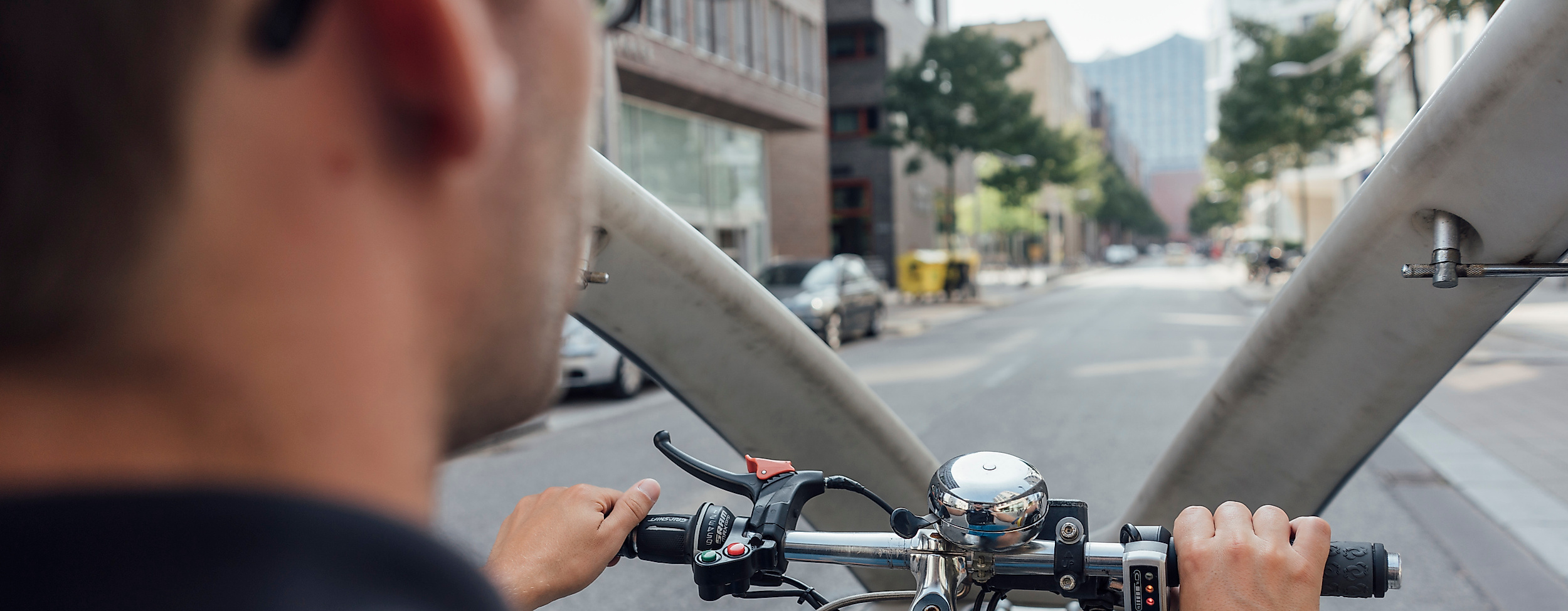 Rikscha-Fahrer aus der Rückansicht steuert durch Hamburger Innenstadtstraße bei Tageslicht.