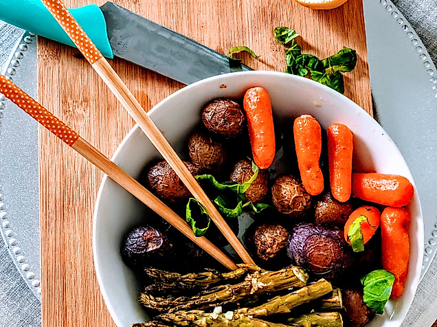 Bunte vegane Bowl mit Gemüse, Falafel und Sesam, serviert auf Holzbrett mit Essstäbchen und Zitrone