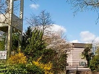 Kirchturm mit grünen Sträucher und im Hindergrund Kirchengebäude