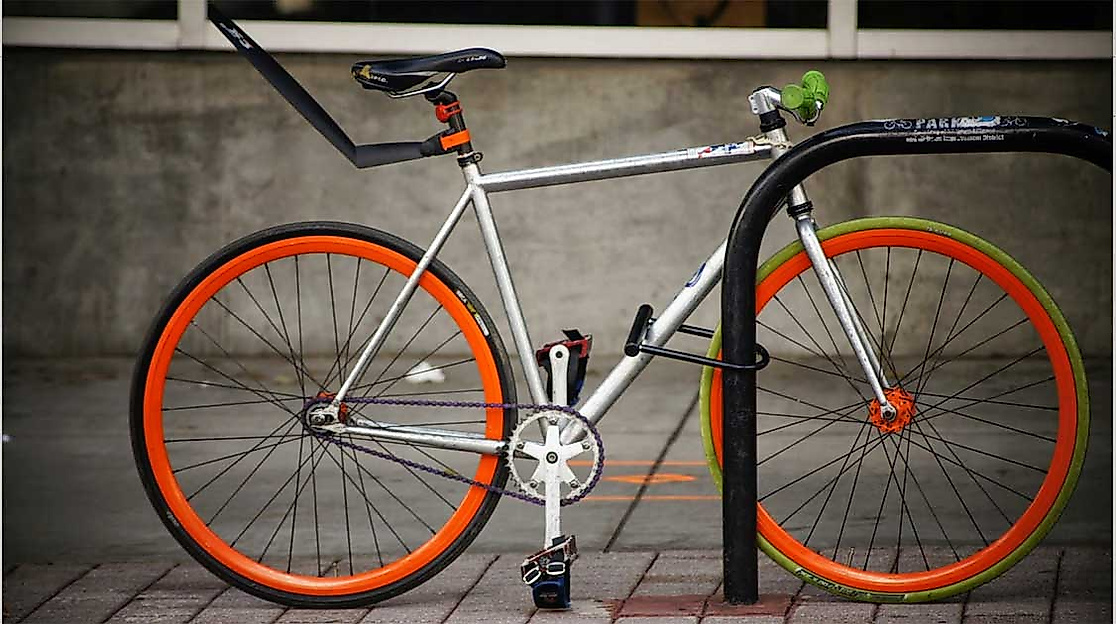 Abgeschlossenes Fahrrad mit orangefarbenen Felgen an Fahrradständer vor Betonwand
