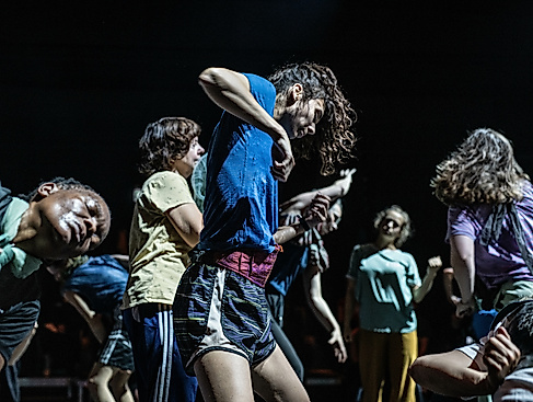 Dancers move intensely and expressively in a tight group formation on stage.