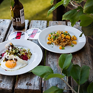Zwei Teller mit norddeutschen Gerichten, darunter Labskaus mit Spiegelei, serviert auf rustikalem Holztisch im Freien.