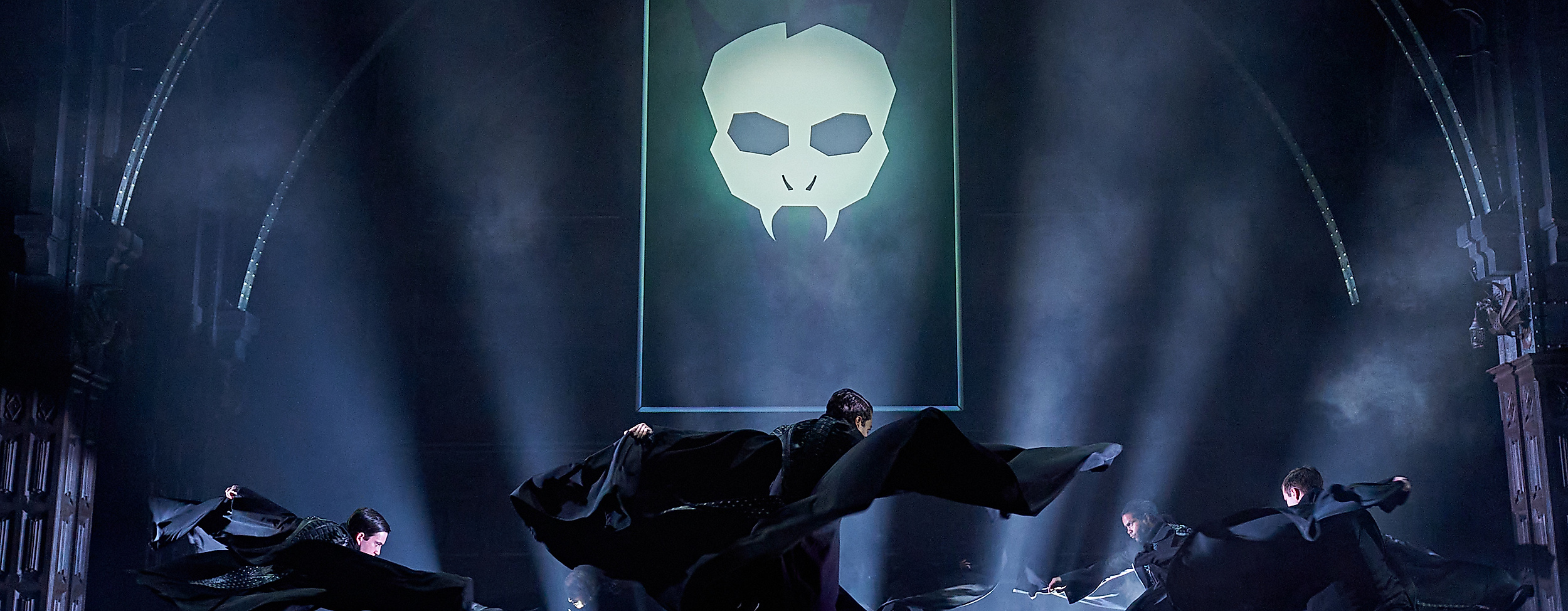 Szenenbild Harry Potter und das verwunschene Kind: Dunkle Atmosphäre, Totenkopf im Hintergrund und Cast beim Tanzen