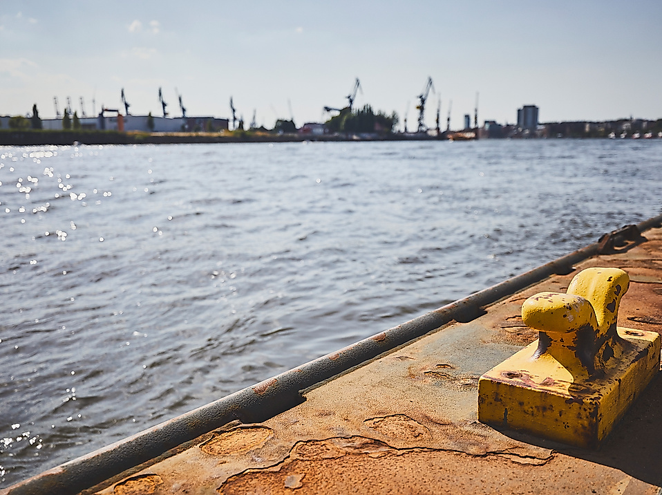 Blick über den Hamburger Hafen mit gelbem Poller im Vordergrund und Werftkränen am gegenüberliegenden Ufer