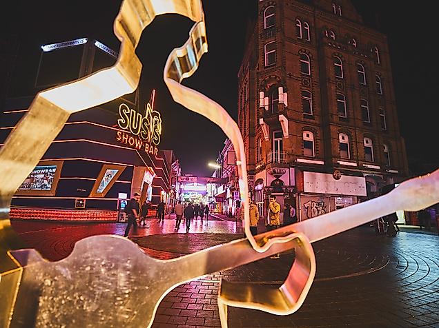 Gitarristen-Skulptur am Beatles-Platz mit Blick in die beleuchtete Große Freiheit bei Nacht