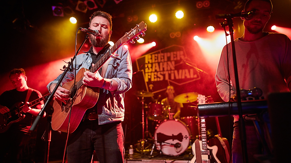 Liveband mit Gitarrist auf rot beleuchteter Bühne beim Reeperbahn Festival in Hamburg
