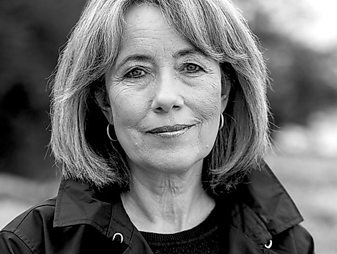 Black-and-white portrait photo of a middle-aged woman with a bob hairstyle. She is wearing hoop earrings and a dark jacket.