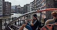 Zwei Personen fahren mit einer Rikscha durch die Hamburger Speicherstadt entlang eines Fleets.