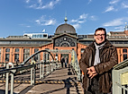 Person auf Brücke vor der Hamburger Fischauktionshalle bei Sonnenschein und blauem Himmel