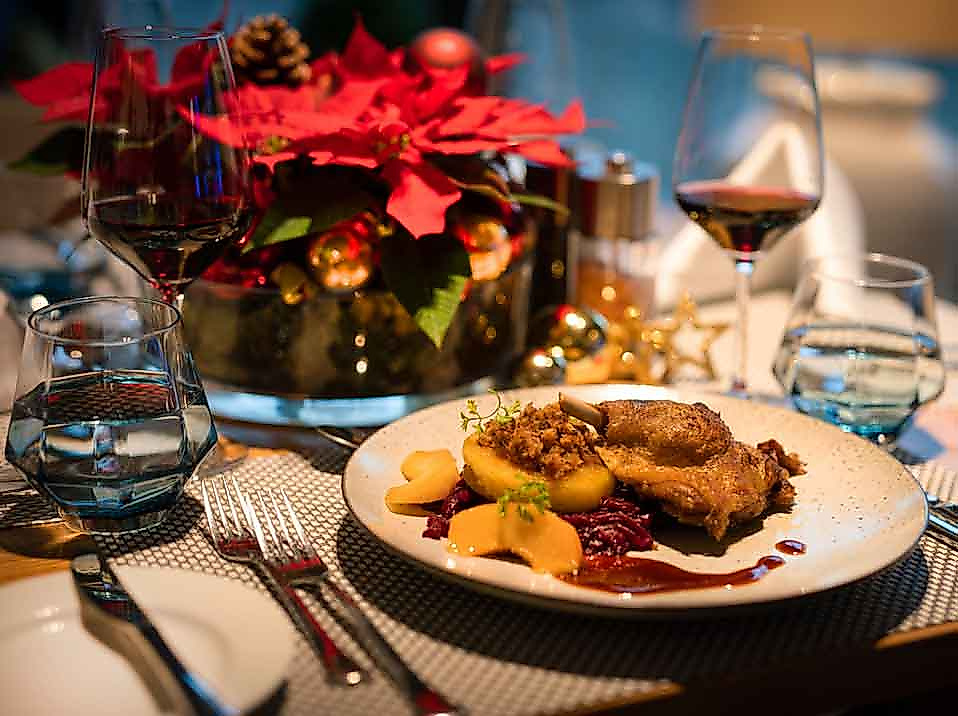 Festlich gedeckter Weihnachtstisch mit Entenbraten, Rotwein und Weihnachtsstern im Kerzenschein